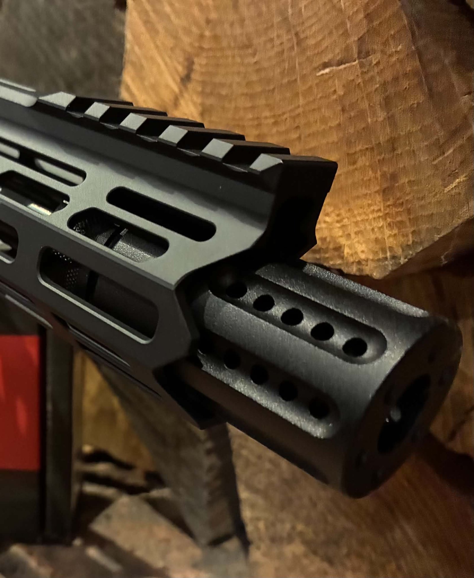 Close-up of the barrel and handguard of the MAPS-AP22 .22LR AR15 Rifle - fully upgraded and match ready, featuring a ventilated muzzle brake, set against a background of wooden planks.